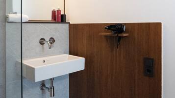 Un baño moderno con cabina de ducha de vidrio, un lavamanos blanco y un mueble de tocador de madera.