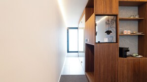 Un pasillo moderno con paneles de madera, un vidrio que da a una habitación luminosa y una cafetera en un estante.