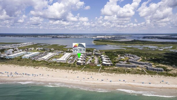 Ett flygbildsfoto av ett bostadskomplex vid kusten, bestående av flera byggnader, en strand och en småbåtshamn.