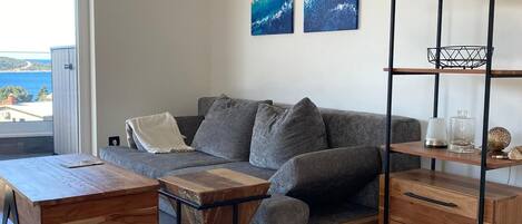 A modern living room with a grey sofa, wooden coffee table, and a wooden side table. There are two abstract paintings on the wall and a red book titled 'FOCUS'.