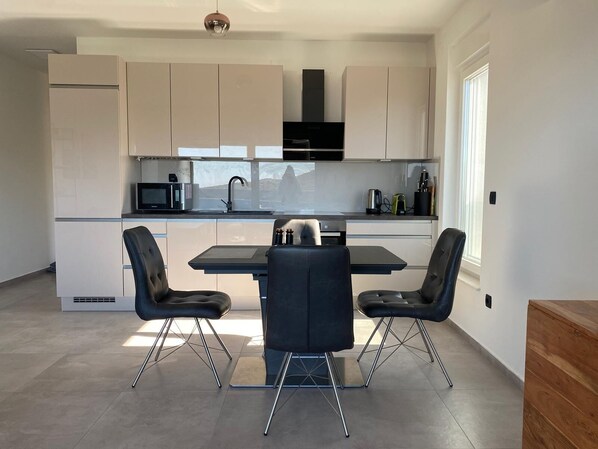 A modern kitchen with a dining table and two chairs, white cabinets, and a black microwave. - Primero Apartment. Quiet, modern, and with an enchanting view of the sea. (Primošten)
