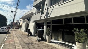 A multi-story building with a modern architectural style, featuring a flat roof and large windows. There are potted plants placed in front of the entrance, and a statue of a lion is visible on the sidewalk. - Renata Palace Hotel (Tubarao)