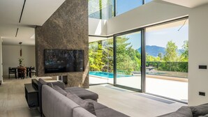 A modern living room with a large flat-screen TV, a grey sectional sofa, and a dining area with a table and chairs. - The Villa O, a unique luxury experience in Sarajevo (Sarajevo)
