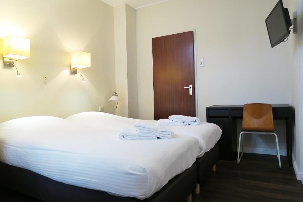 Ein Hotelzimmer mit einem Bett, zwei Nachttischlampen, einem Schreibtisch mit Stuhl und einem an der Wand befestigten Fernseher.