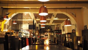 A restaurant interior with high ceilings, exposed beams, and multiple hanging pendant lights. - Hotel Carillon (Haarlem)