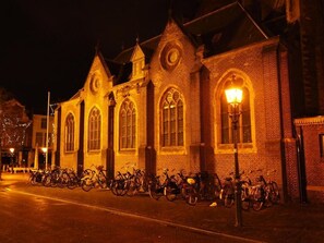 A brick building with arched windows and a clock tower, lined with bicycles.