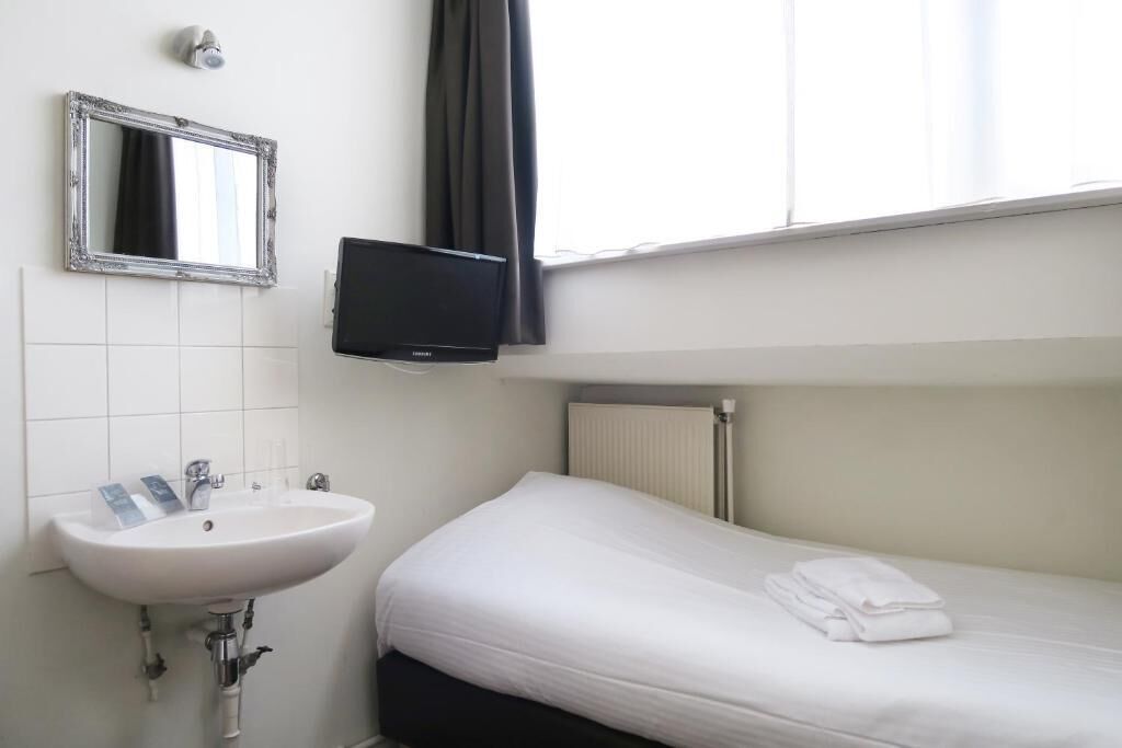 A hotel room with a white sink, a mirror, a flat-screen TV, a bed with white bedding, and a window with curtains.
