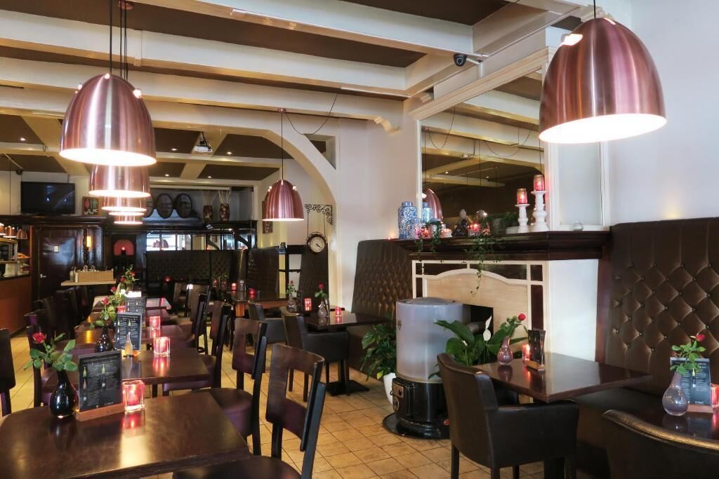 A restaurant with wooden tables and chairs, pendant lighting, and a bar area with stools.