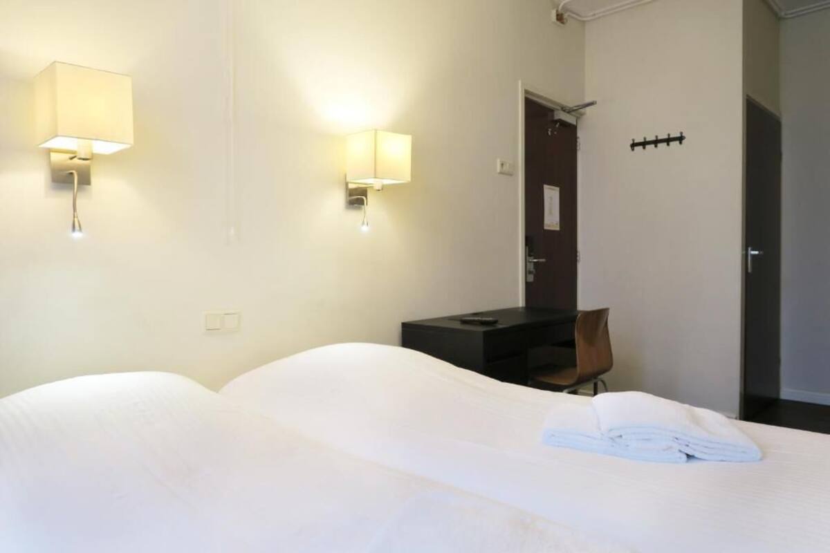 A hotel room with two beds, a desk, and two wall-mounted lamps.