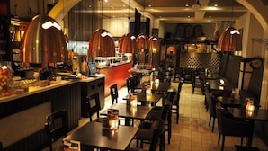A restaurant with multiple tables and chairs, a bar area, and pendant lighting. - Hotel Carillon (Haarlem)