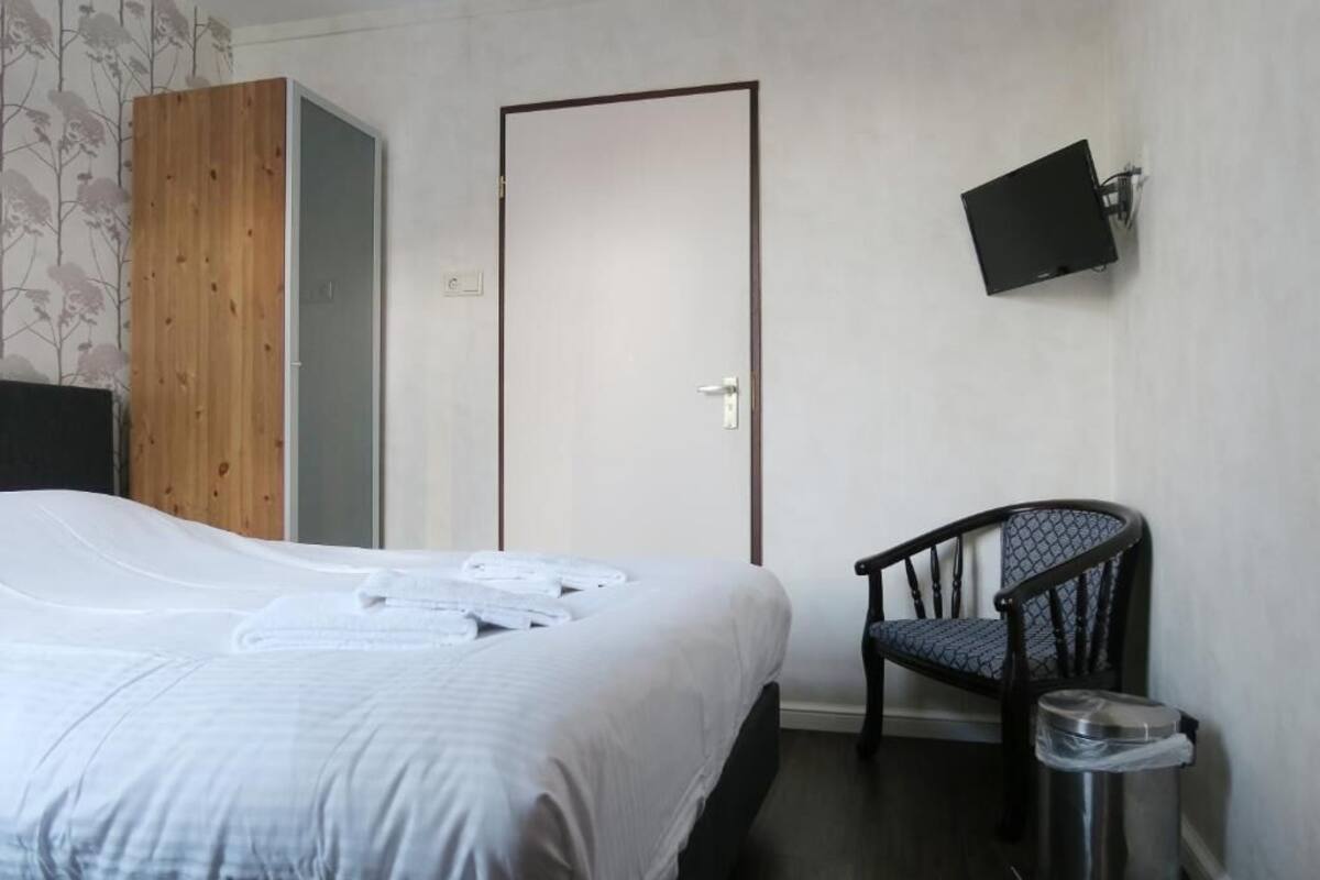 A hotel room with a bed, a chair, a television mounted on the wall, and a door.