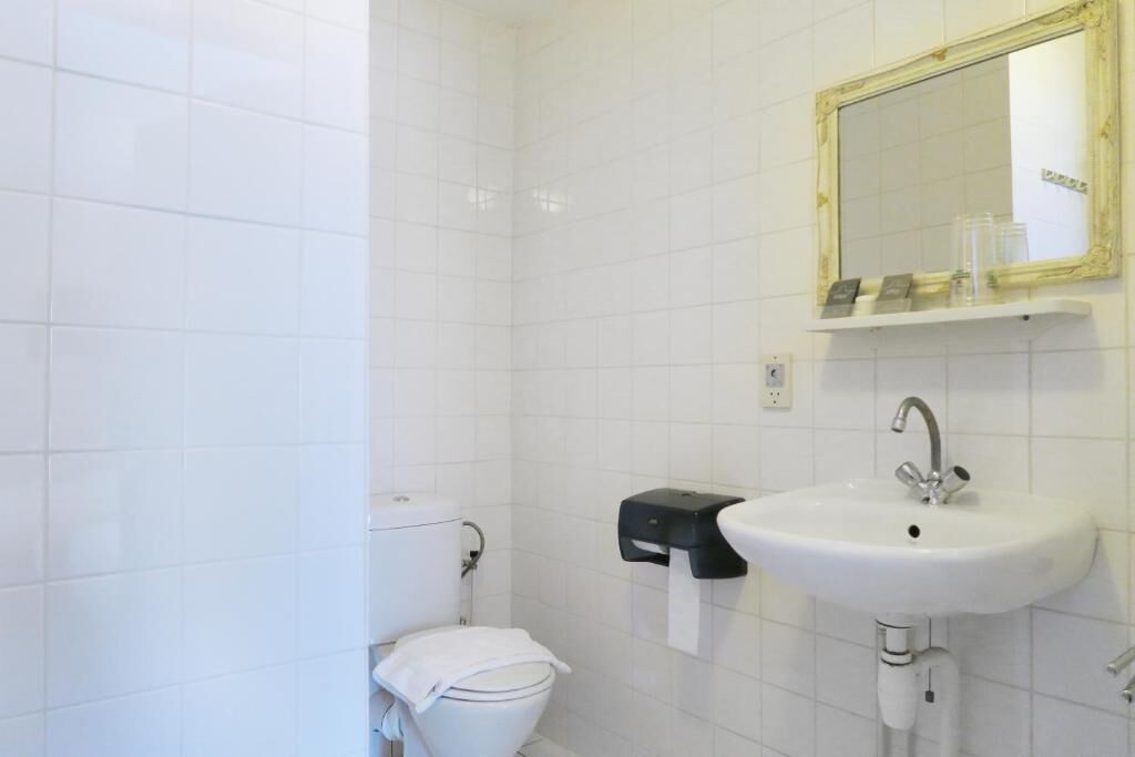 Een badkamer met witte betegelde wanden, een wit toilet, een wastafel met een spiegel erboven en een papieren handdoekdispenser.