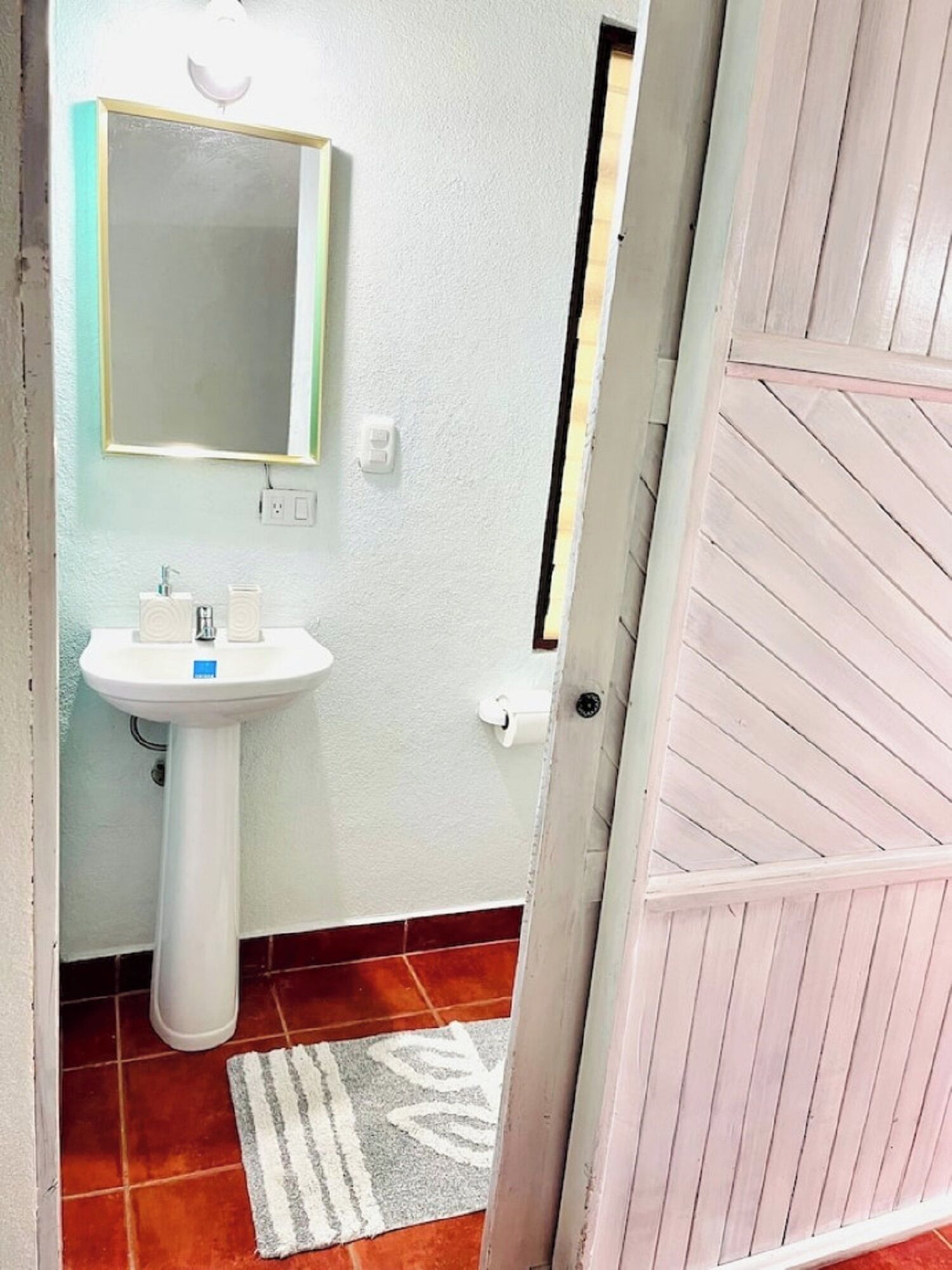 A bathroom with a white pedestal sink, a mirror, and a towel rack.