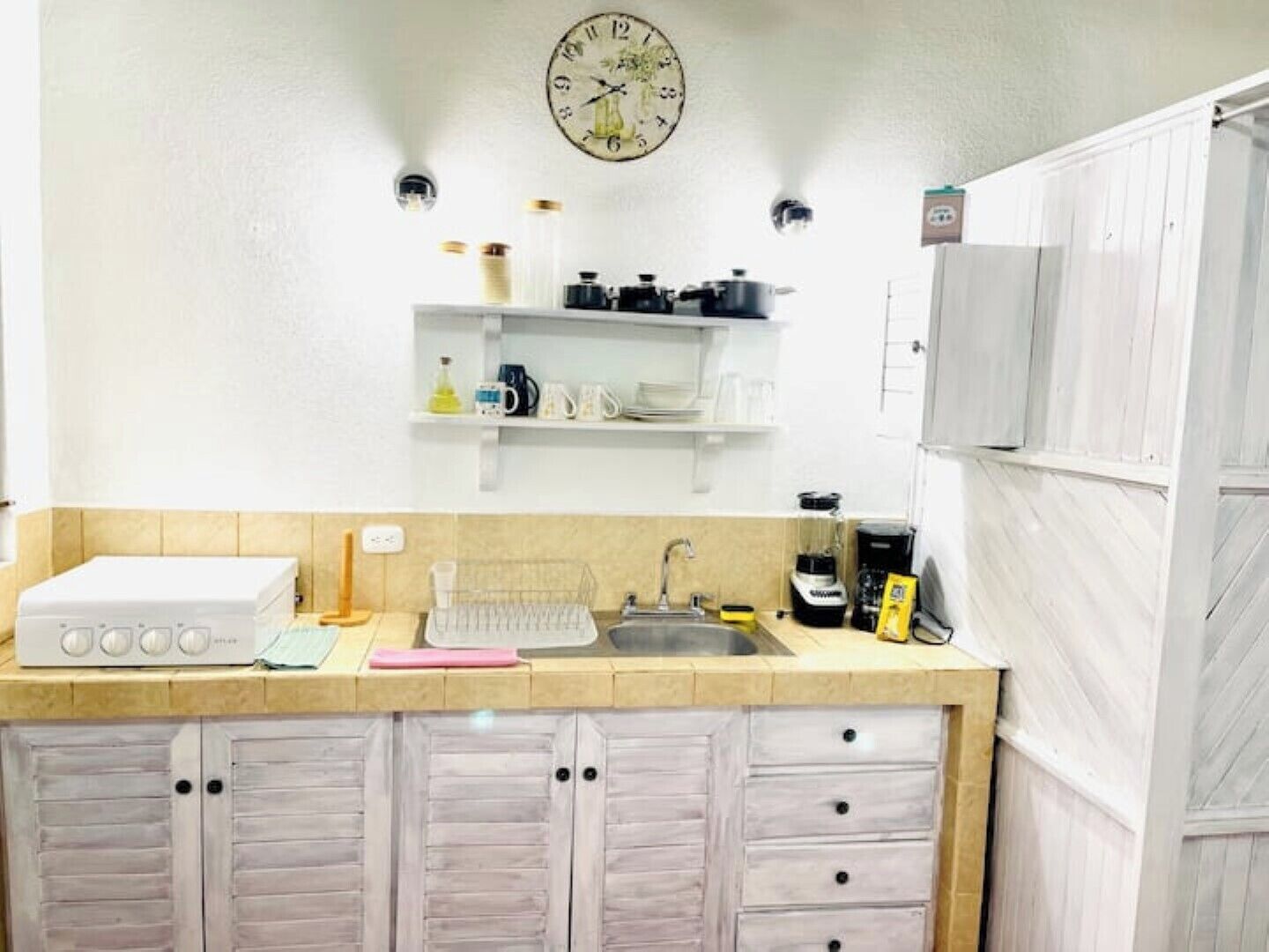 A kitchen with a white countertop, a sink, a coffee maker, and a clock on the wall.