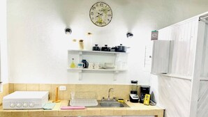 Eine Küche mit weißer Arbeitsplatte, einem Spülbecken, einer Kaffeemaschine und einer Uhr an der Wand.
