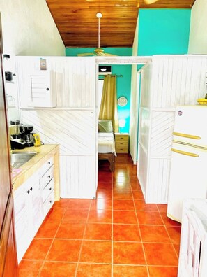 Une cuisine de taille réduite avec des meubles blancs, un plafond en bois et un sol carrelé.