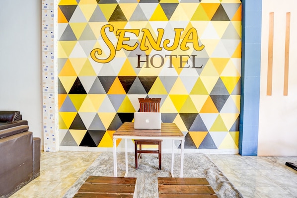A room with a geometric patterned wall, a wooden table with a laptop, and a brown leather sofa.