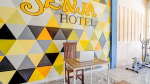 A room with a geometric patterned wall, a wooden chair, a table with a laptop, and exercise equipment. - Hotel O Senja Syariah (Gresik)