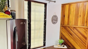 Eine kompakte Küche mit Kühlschrank, einem Fenster mit Jalousien, einem Holzessttisch mit Stühlen und einem an der Wand befestigten Schild.