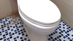 A toilet with a white tank and lid, set against beige tiled walls and a blue and white checkered floor. - OYO Life  92842 Homestay Balearjosari (Malang)