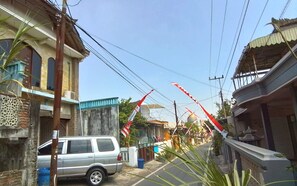 Une rue étroite, bordée de bâtiments des deux côtés, avec une voiture garée et des drapeaux rouges.