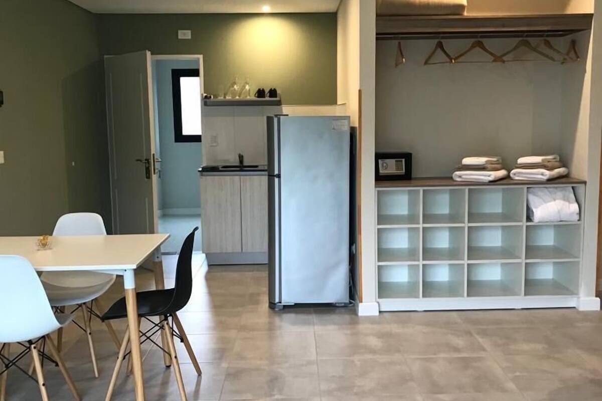 Une cuisine moderne dotée d’un réfrigérateur encastré, d’un coin repas avec une table et des chaises, et d’un dressing avec des étagères.