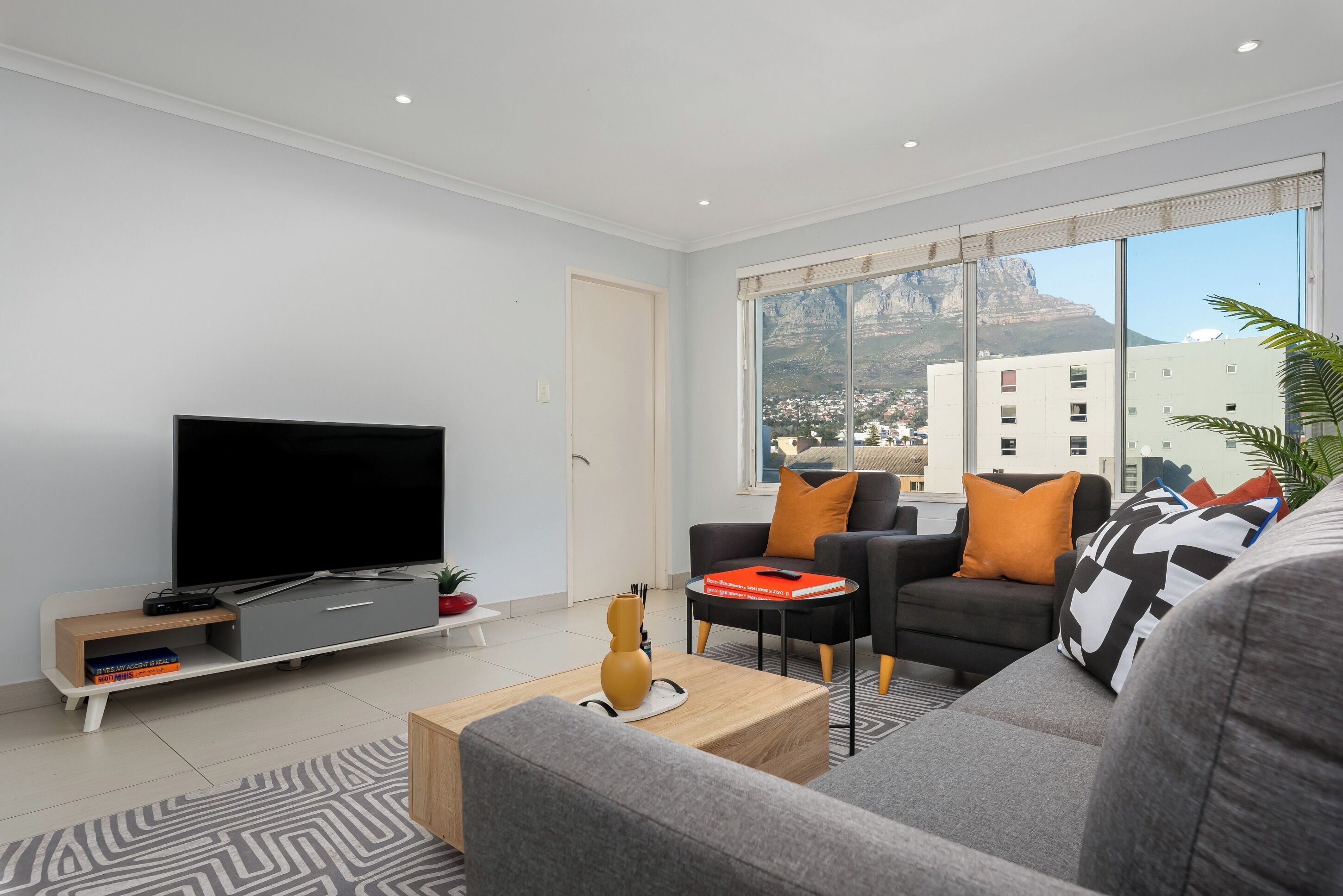 Una sala de estar moderna con un televisor de pantalla plana, sofás grises, una mesa de centro y un ventanal con vistas a la ciudad.