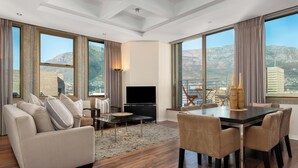 A modern living room with a sofa, TV, and dining table, large windows with mountain views, and a cityscape in the background. - Modern & Open 2BR with Table Mountain & Lions Head Views
 (Cape Town)
