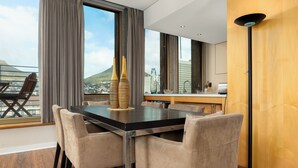 A modern dining area with a large table, cushioned chairs, and a view of a cityscape and mountain. - Modern & Open 2BR with Table Mountain & Lions Head Views
 (Cape Town)