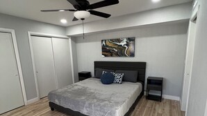Ein modernes Schlafzimmer mit Bett, Deckenventilator, Kunstwerken und Holzboden.