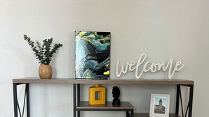 Ein Holzkonsolentisch mit einem 'welcome'-Schild, einem gerahmten Bild und Dekorationselementen.