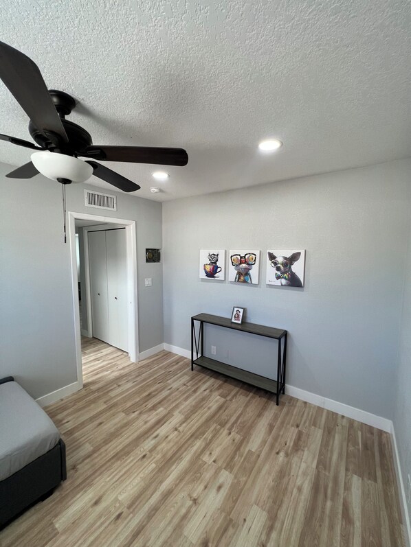 Una stanza con una ventola a soffitto, un comodino con una cornice e una porta che dà su un'altra stanza.