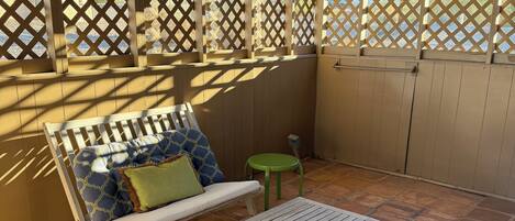 An outdoor patio with a wooden bench, a small table, and a green stool.