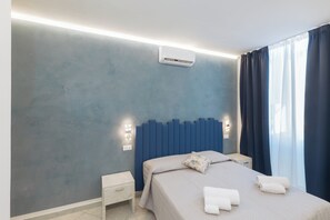 A modern bedroom with a bed, bedside tables, an air conditioner, and a window with curtains. - AFFITTACAMERE ELENA (Sanremo)