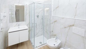 Une salle de bain moderne avec une douche à parois de verre, un lavabo blanc et un bidet.