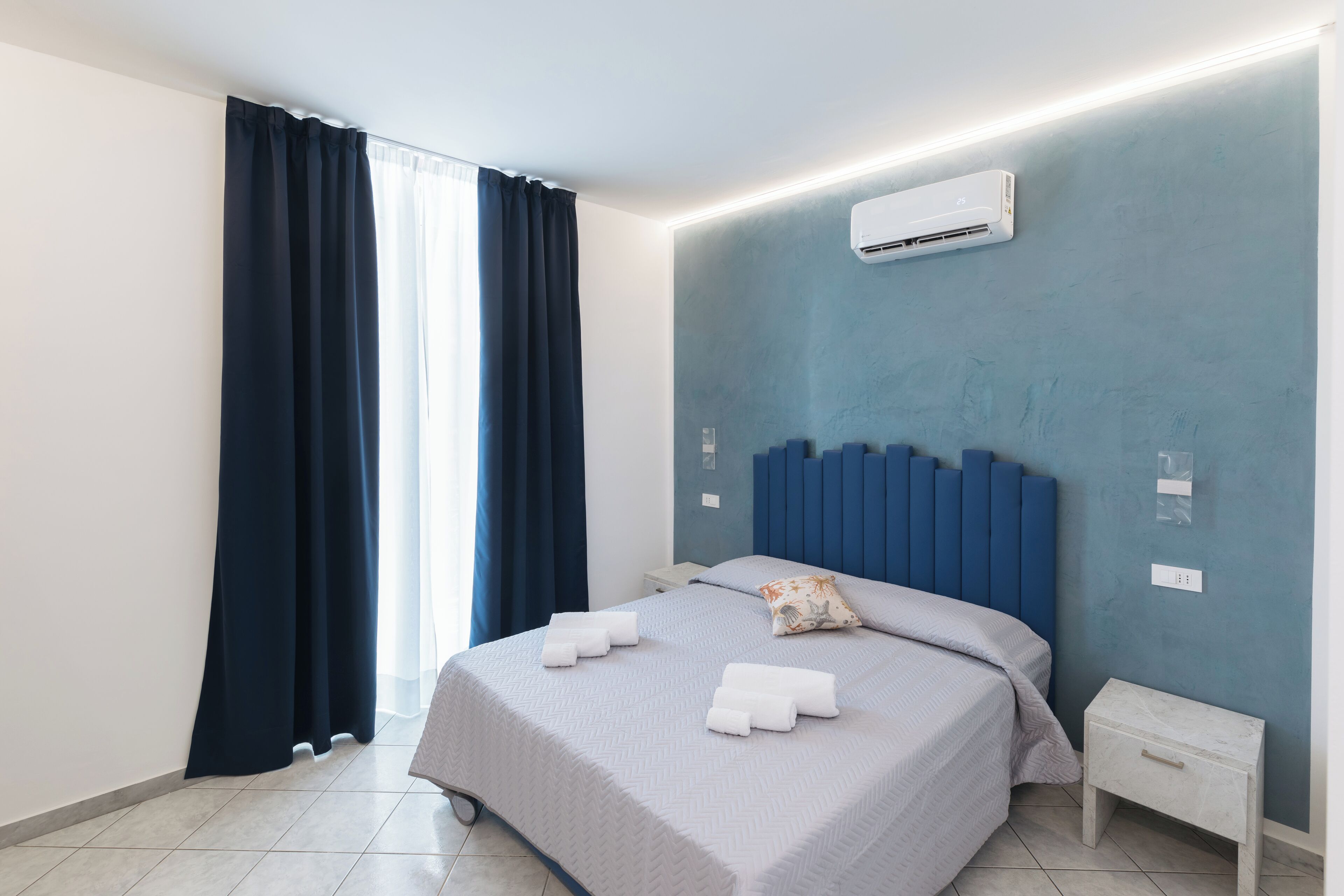 Une chambre d’hôtel moderne équipée d’un lit, d’une table de chevet et d’un appareil de climatisation fixé au mur.