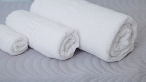 Trois serviettes blanches roulées sont posées sur un lit recouvert d’une courtepointe blanche à motifs.