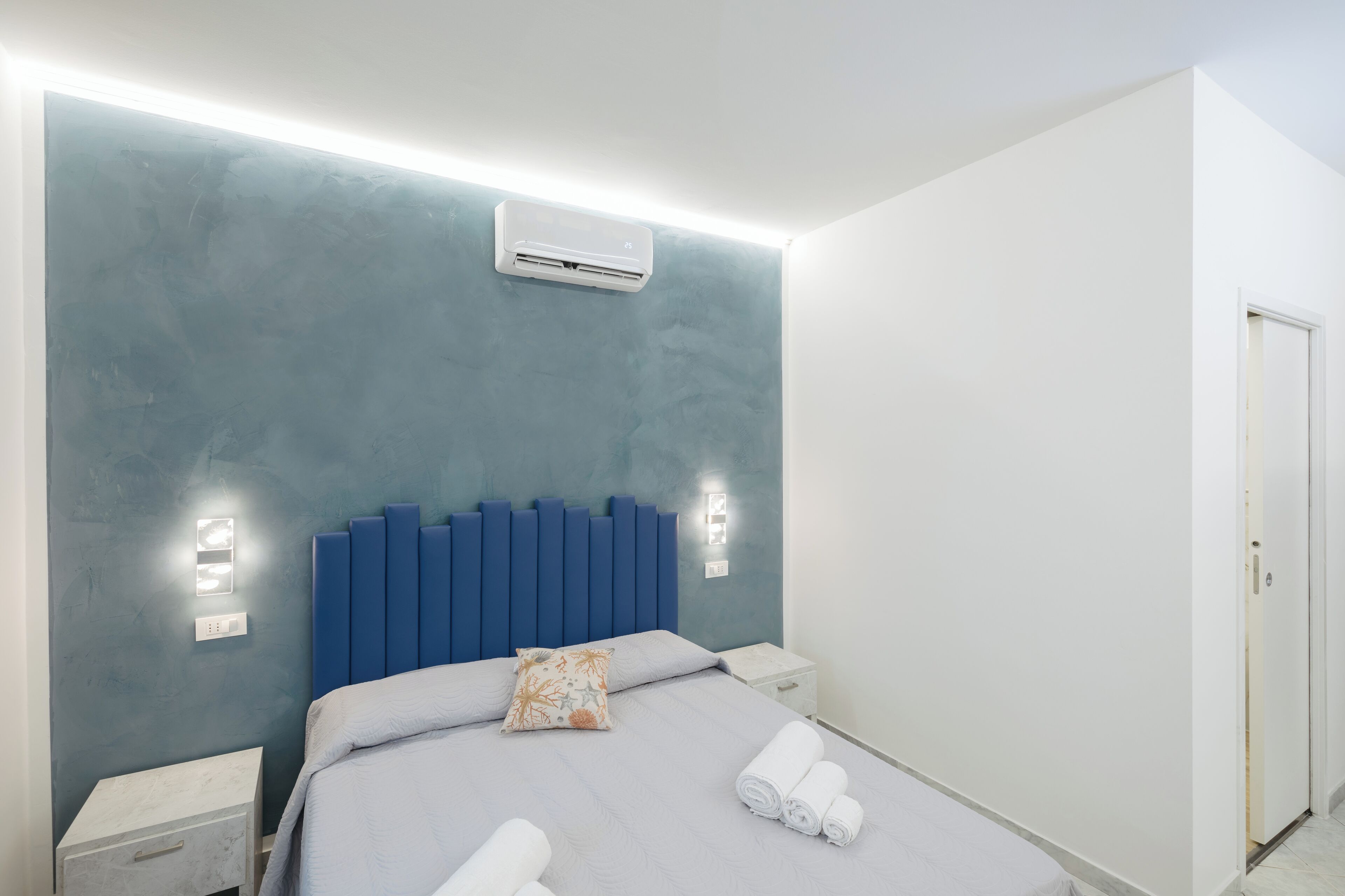 Un dormitorio moderno con cabecera azul, lámparas de noche y toallas ordenadas.