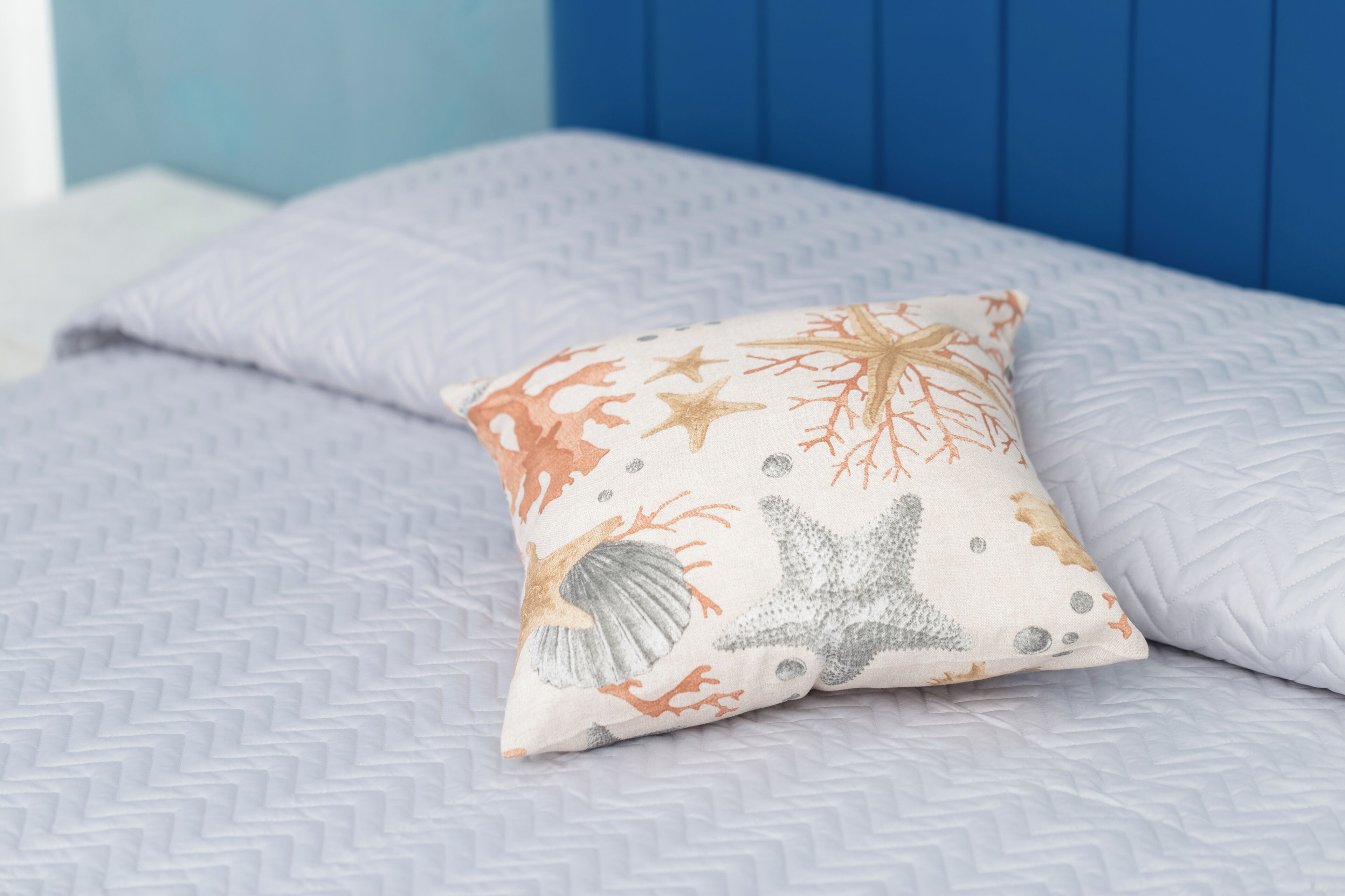 Un letto con una coperta a motivi e un cuscino decorativo a tema marino.