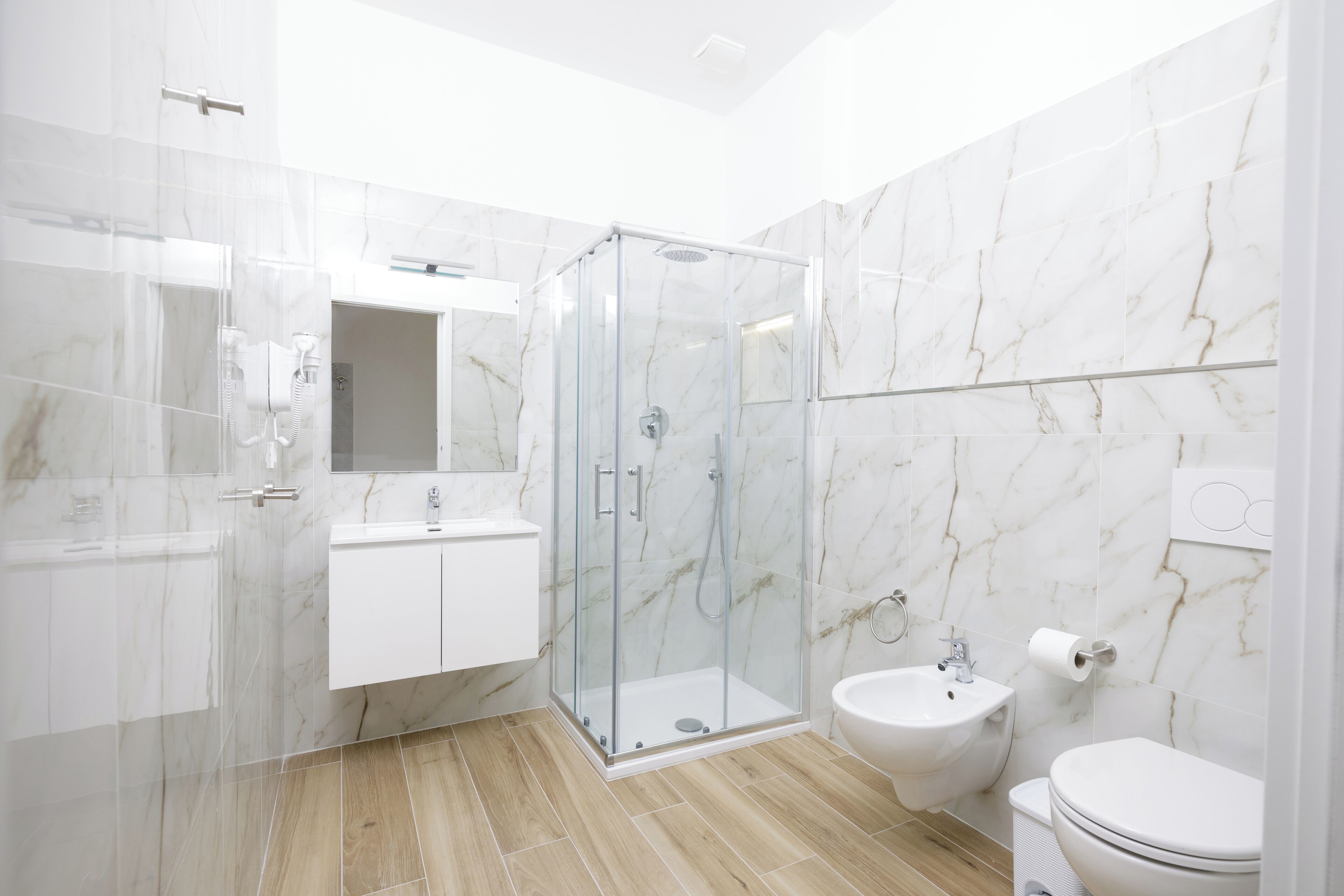 A modern bathroom with a glass-enclosed shower, a white sink, and a bidet.