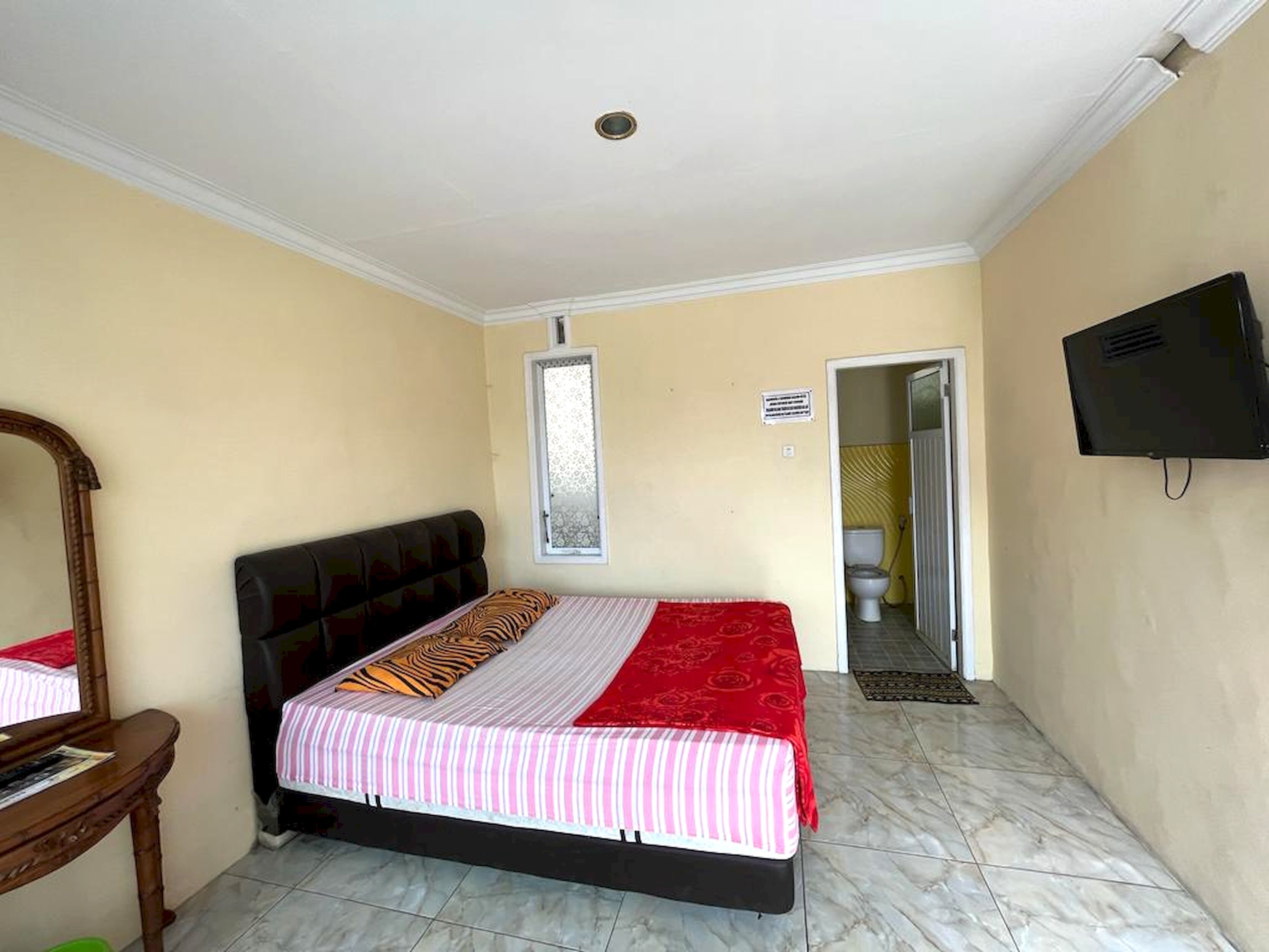 A bedroom with a bed, a wooden dresser, a television, and a bathroom door.
