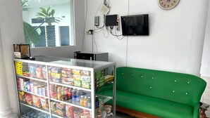 Un espace d’accueil avec un présentoir en verre rempli de collations et de boissons, un canapé vert et une horloge au mur.