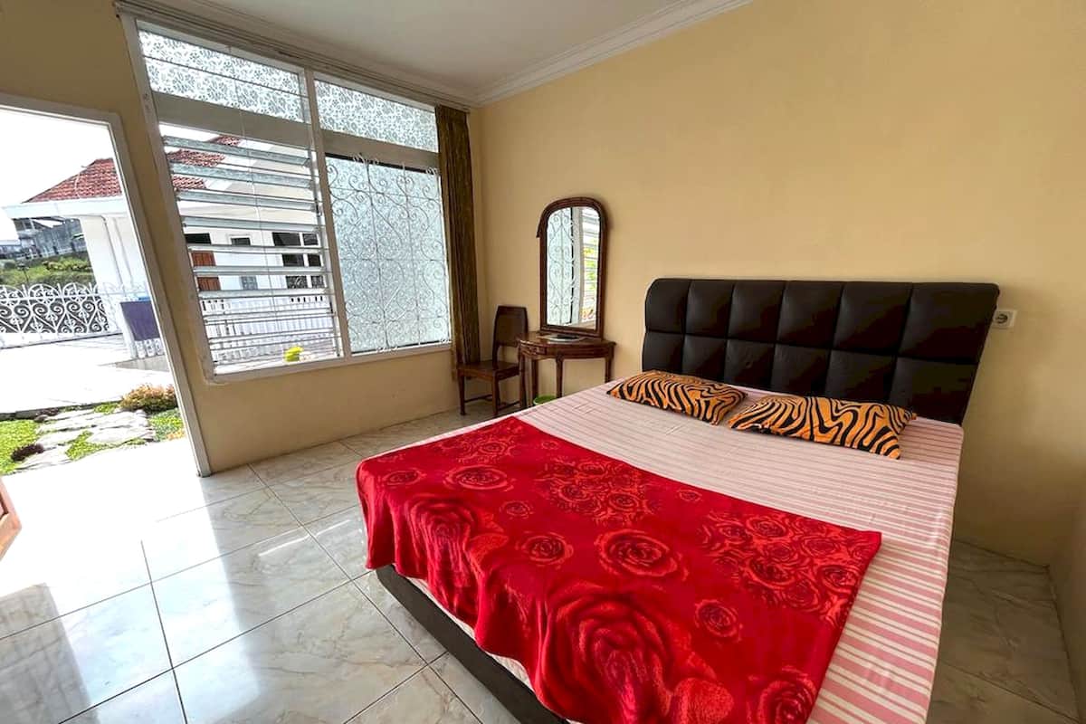 Ein Schlafzimmer mit Bett, Stuhl, Schreibtisch und Fenster mit Blick auf ein Gebäude und einen Zaun.