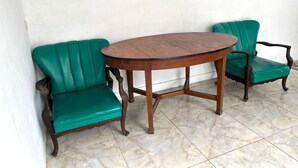 Une pièce avec une table ronde en bois et deux chaises recouvertes d’un tissu vert.