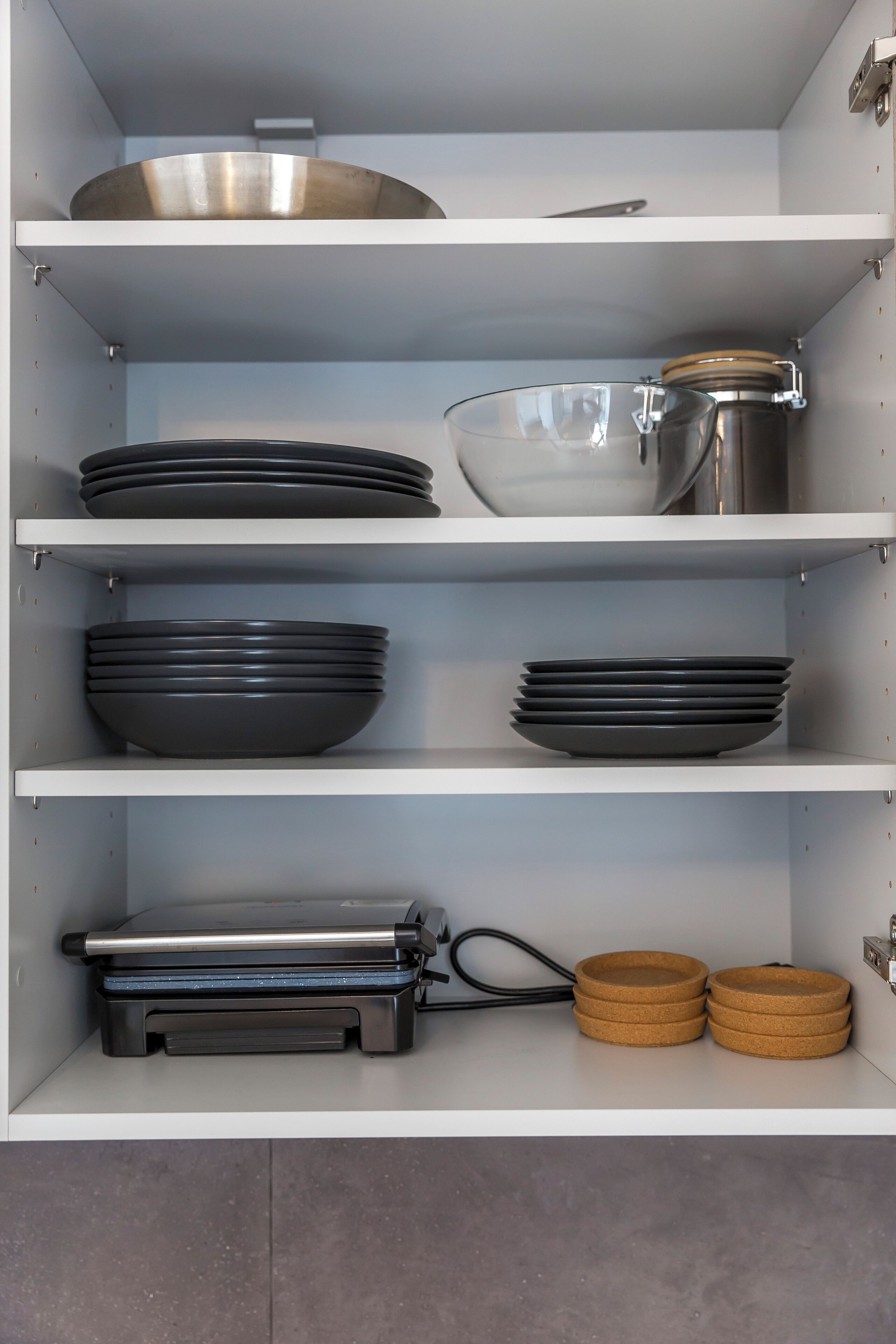 A kitchen cabinet with shelves holding plates, bowls, a pot, and a toaster.