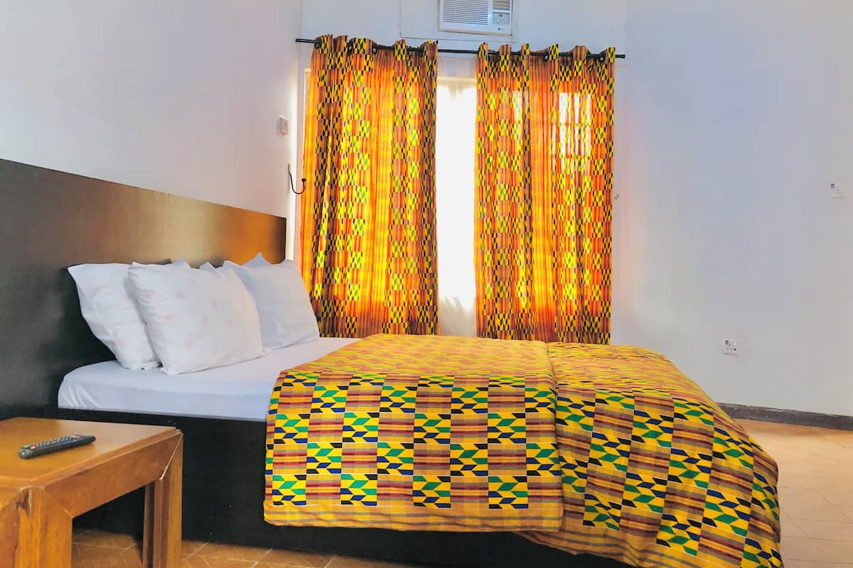 Una habitación de hotel con una cama, una mesita de noche de madera, un control remoto y cortinas estampadas.