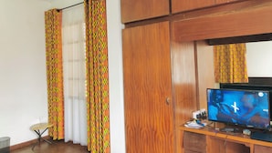 Une pièce dotée d’un ventilateur de plafond, de meubles en bois, d’un téléviseur et de rideaux à motifs.