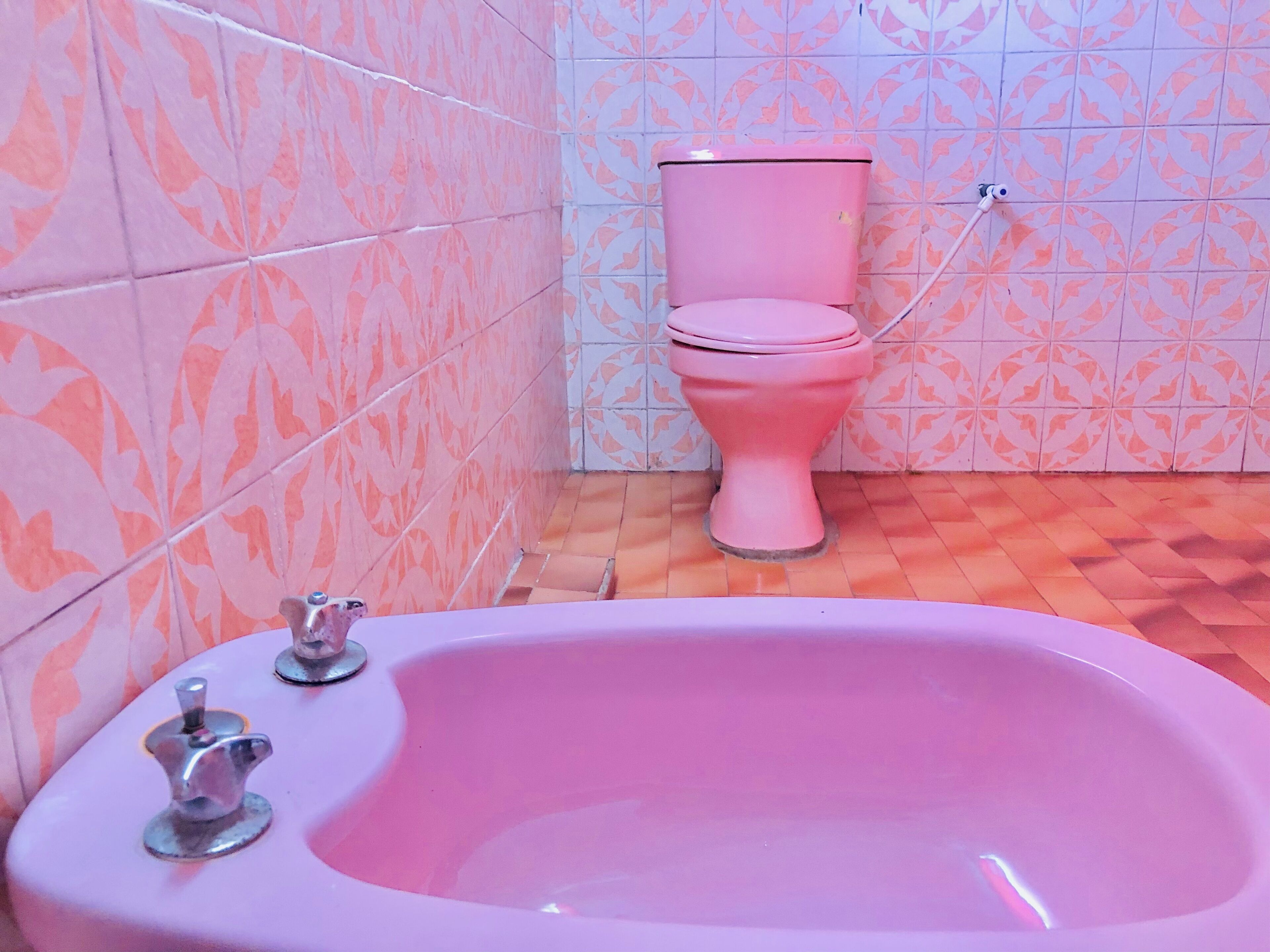 Une salle de bain avec une baignoire rose, des toilettes roses et des carreaux à motifs.