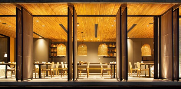 A restaurant with wooden ceiling and walls, multiple dining tables, and chairs.