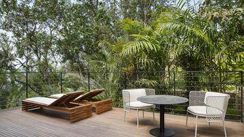 Una terraza de madera con una silla de descanso, dos sillas blancas y una mesa redonda.